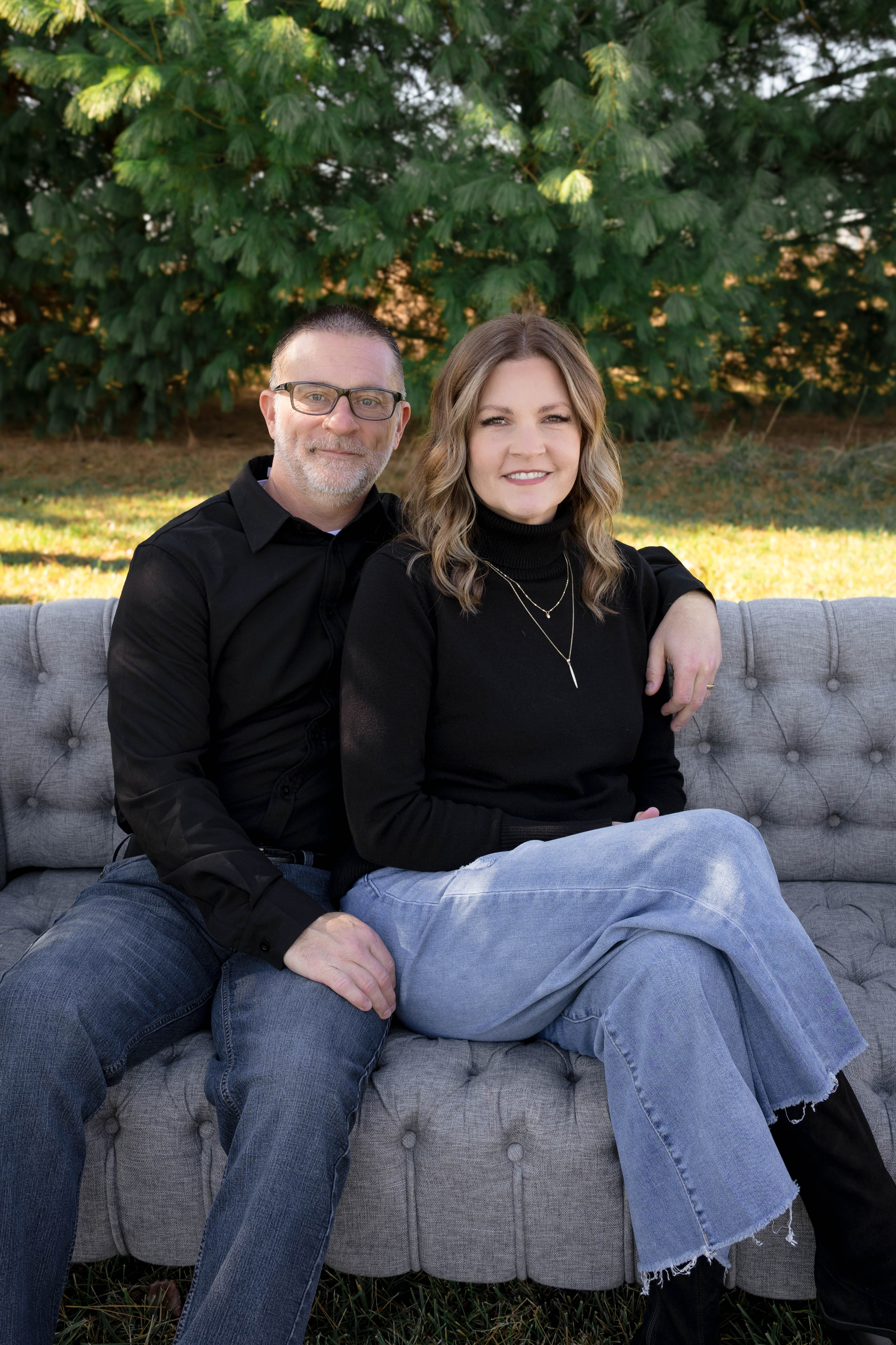 Tracy and Chad Bramel seated on a gray couch outdoors, founders of the faith-based brand A Moved Heart Collective